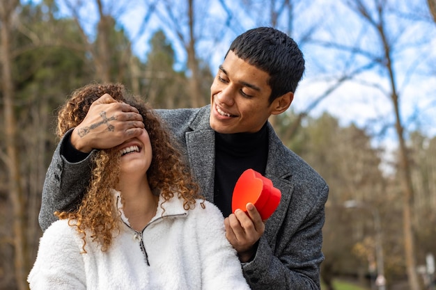 Latin man on valentine39s day covering her boyfriend39s eyes sitting outdoors valentine39s day