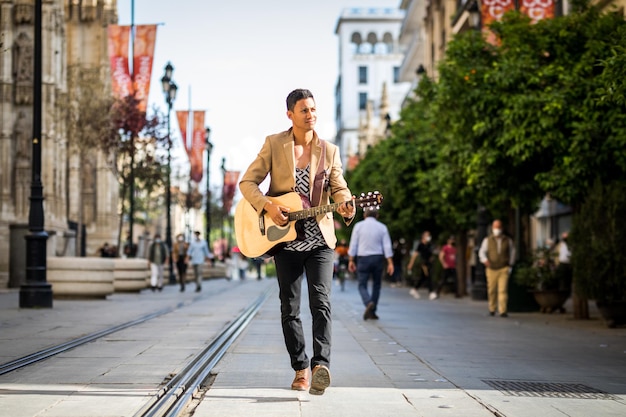 Latin man walking while playing guitar on busy street (landscape)