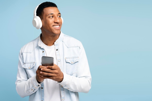 Latin man wearing headphones holding smartphone listening music and looking away