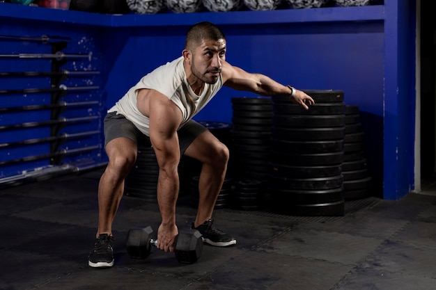 Latin man with sportswear doing exercises with dumbbell in the gym