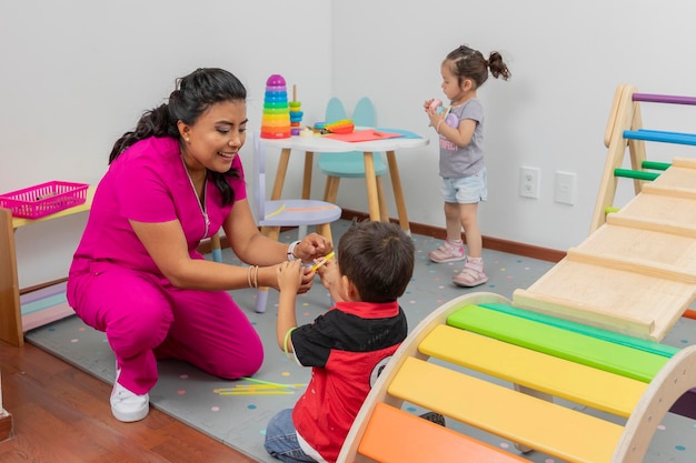 Latin pediatrician playing with a child in her medical office while a girl plays on a table in the background