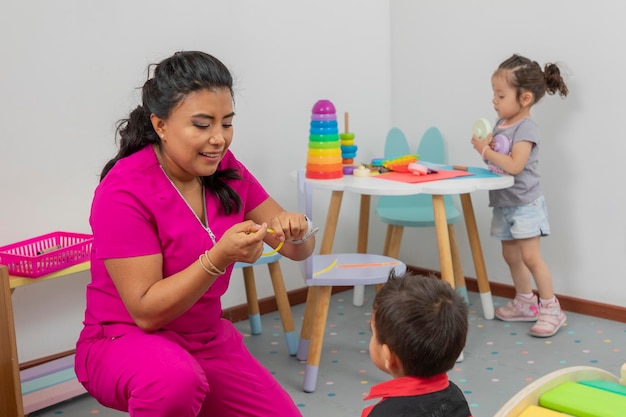 Latin pediatrician playing with a child in her medical office while a girl plays on a table in the background