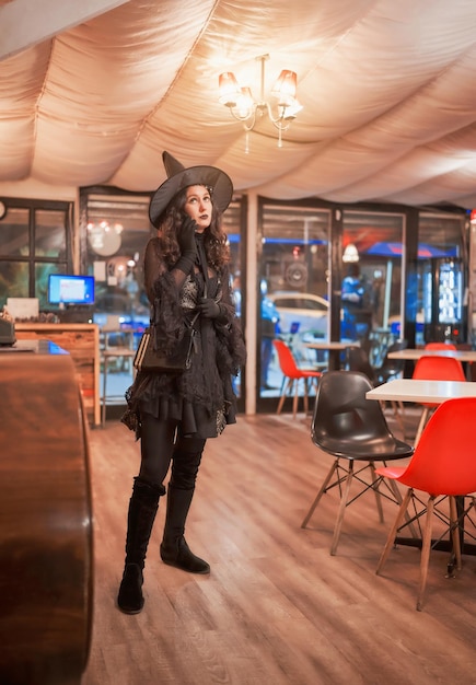 Latin woman dressed as a witch in a cafe or restaurant standing and talking on the cell phone