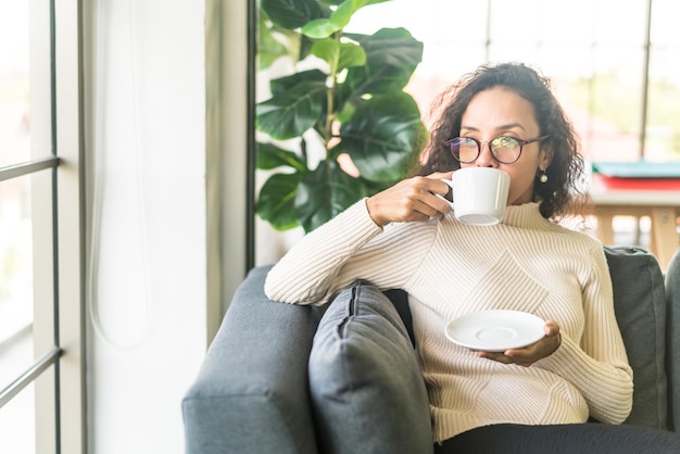 Latin woman drinking coffee on sofa at home