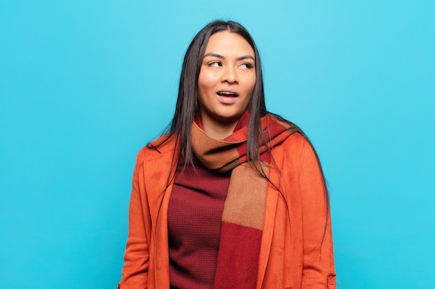 Latin woman feeling shocked, happy, amazed and surprised, looking to the side with open mouth