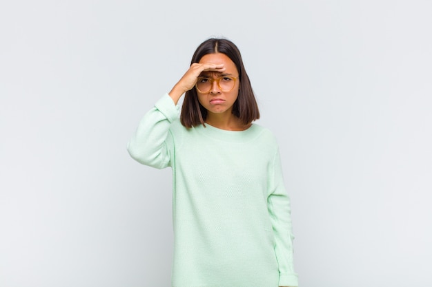 Latin woman looking bewildered and astonished, with hand over forehead looking far away, watching or searching