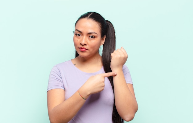 Latin woman looking impatient and angry, pointing at watch, asking for punctuality, wants to be on time