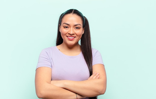 Latin woman looking like a happy, proud and satisfied achiever smiling with arms crossed