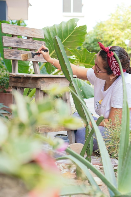 Latin woman painting wooden chairs in garden