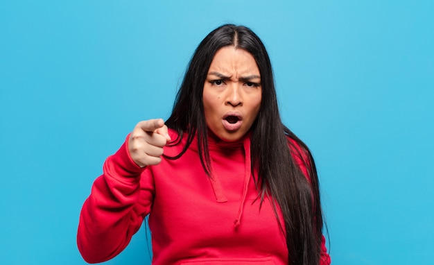 Latin woman pointing with an angry aggressive expression looking like a furious, crazy boss