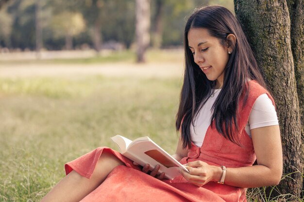 Latin woman reading an ornate book of a tree in the park