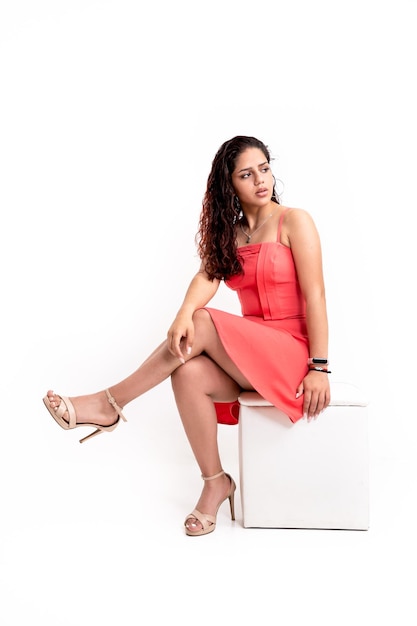 Latin woman in salmon colored dress sitting in white pub on white background