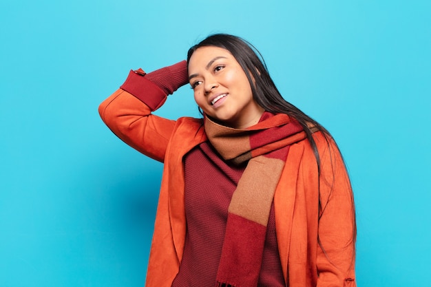 Latin woman smiling cheerfully and casually, taking hand to head with a positive, happy and confident look