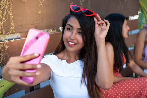 Latin woman taking a selfie for social media while enjoying an afternoon with friends