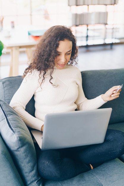 Latin woman using laptop and hand holding credit card for shopping on sofa at home