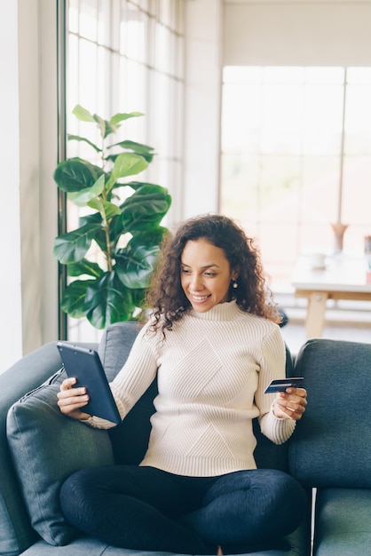 Latin woman using tablet and hand holding credit card