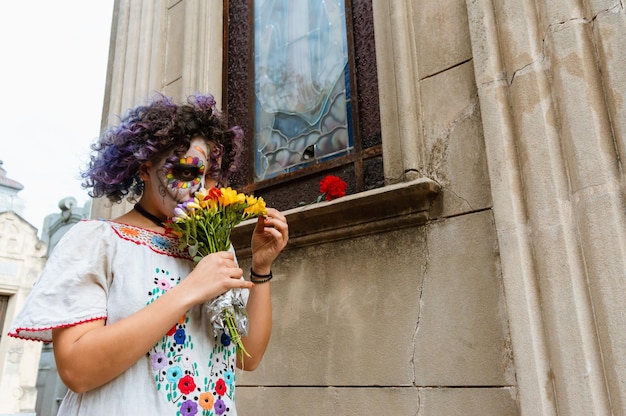 Latin young woman in the cemetery with Catrina makeup placing flowers on an altar of the virgin