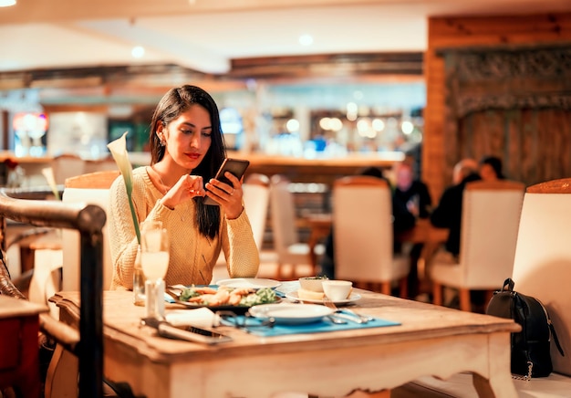 Latin young woman sitting alone in a restaurant using smartphone x9