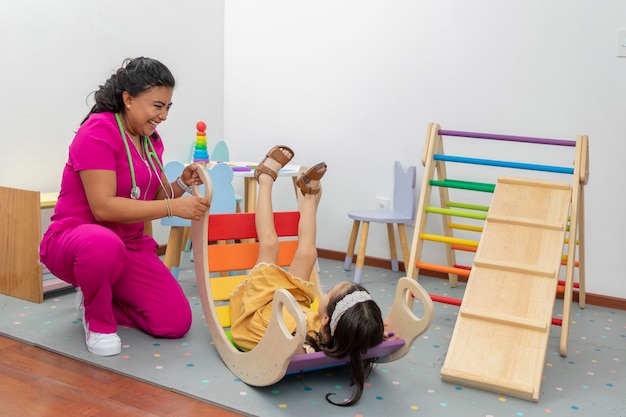 Latina pediatric doctor laughing while playing with a girl in the play area of her office