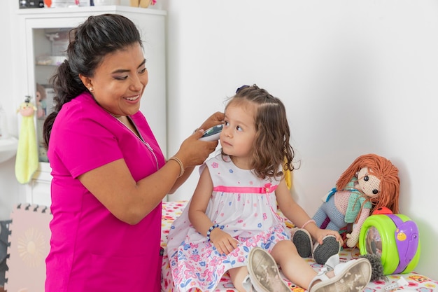 Latina pediatrician doctor checking the ear of a girl in her office