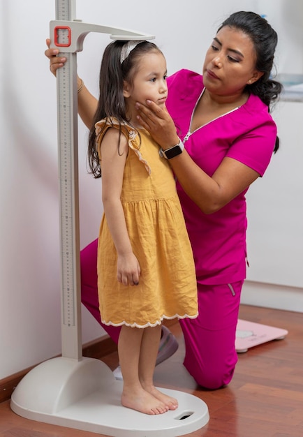 Latina pediatrician doctor measures a girl in her office with a pedestal ruler