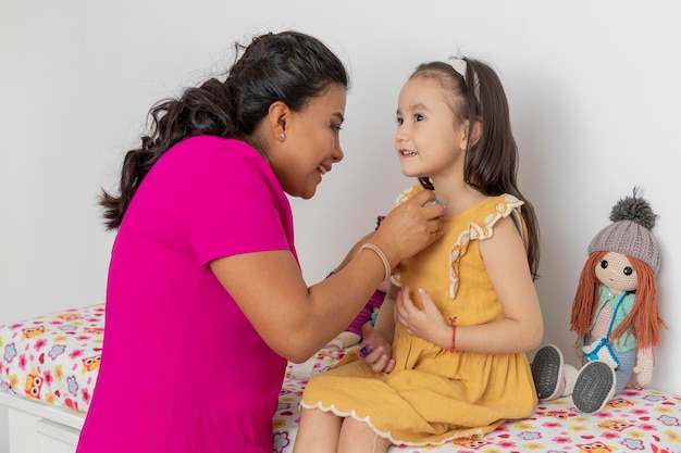 Latina pediatrician doctor placing a BandAid on a girl who is sitting on the bed in her office