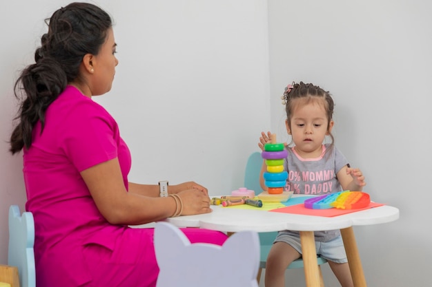 Latina pediatrician doctor sitting at a table with a little girl playing in the game room of her medical office