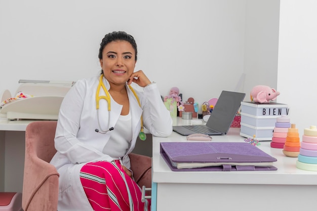 Latina pediatrician sitting at her desk wearing a lab coat and with a stethoscope around her neck