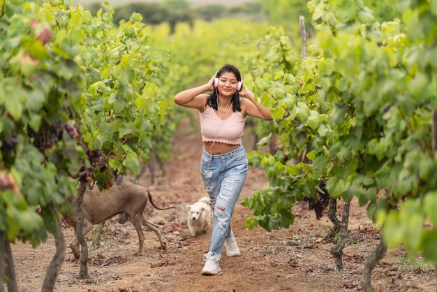 Latina woman listening to music while walking among vineyards