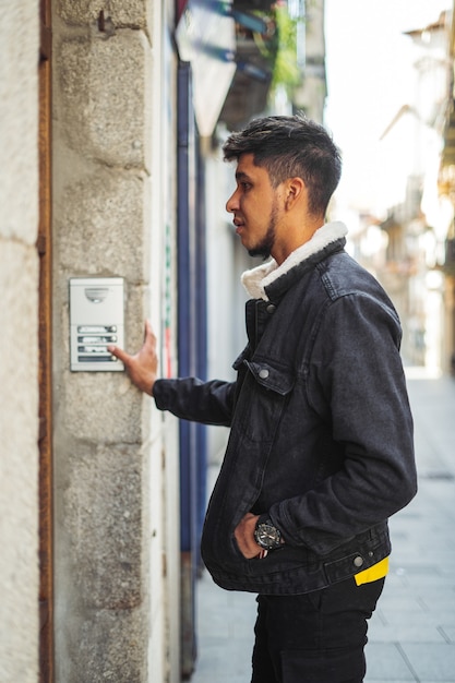 Latino man ringing a building doorbell