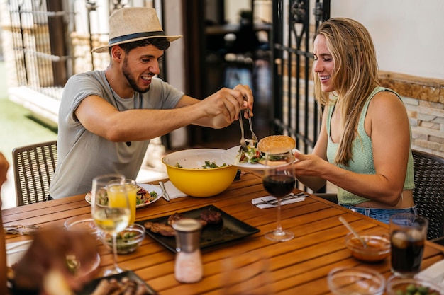 Latino man in sombrero tosses some salad as a hamburger to a blonde Caucasian woman