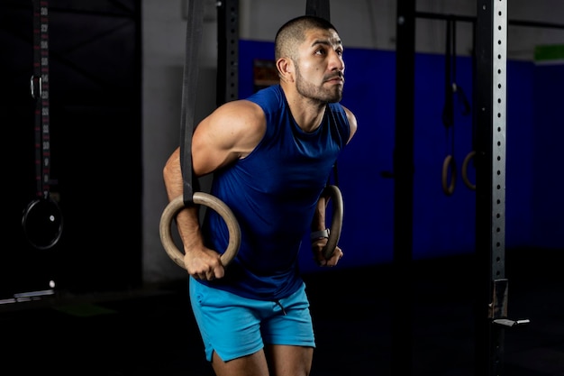 A Latino man in sportswear doing gymnastic exercises on some rings in a gym