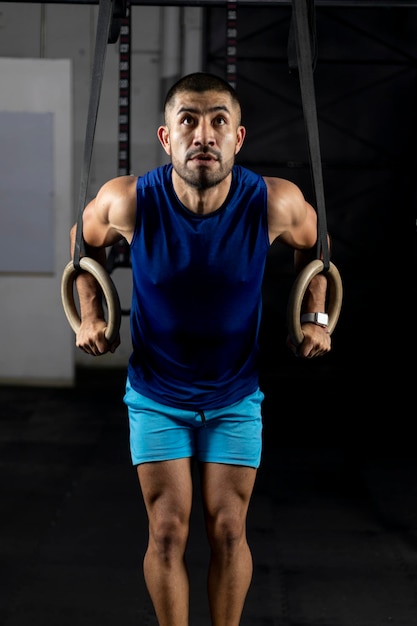 A Latino man in sportswear doing gymnastic exercises on some rings in a gym