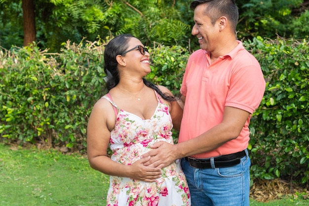 Latino man touching his pregnant wife39s belly while they are together in the backyard of their home