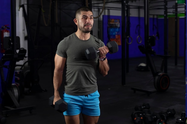 Latino man with sportswear doing biceps exercises with two dumbbells in a gym