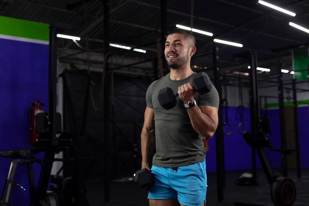 Latino man with sportswear doing biceps exercises with two dumbbells in a gym