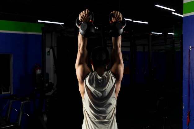 Latino man with sportswear doing press with a pair of kettlebells in a gym