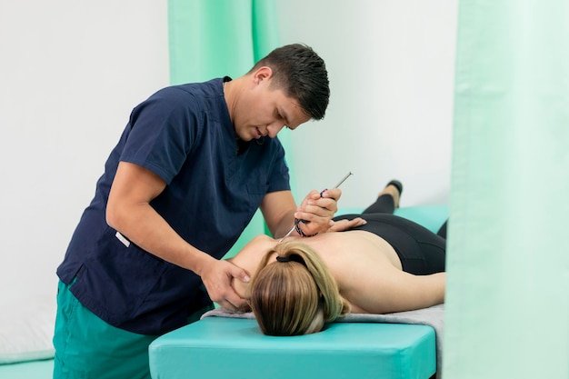 Latino physiotherapist doctor applies a treatment for fibrolysis to his female patient lying face do