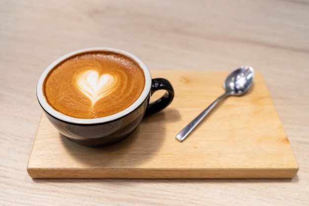 Latte coffee or cappuccino coffee in black cup with beautiful heart latte art on wooden table