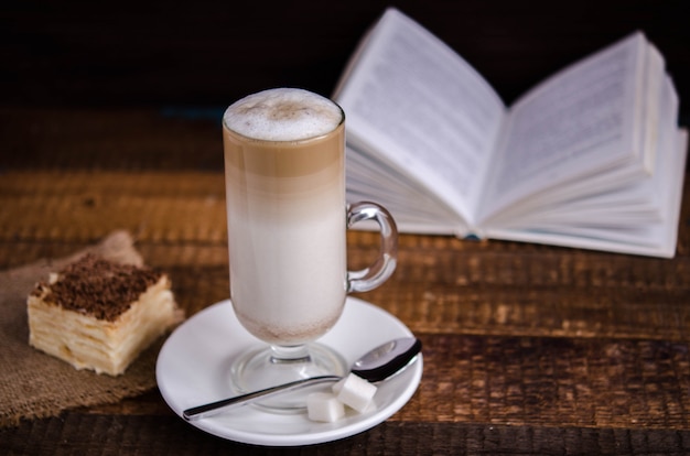 Latte coffee drink in a glass cup with a book in the background