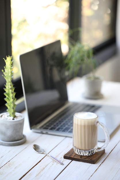 Latte coffee and notebook with plant pot on desk in front of window