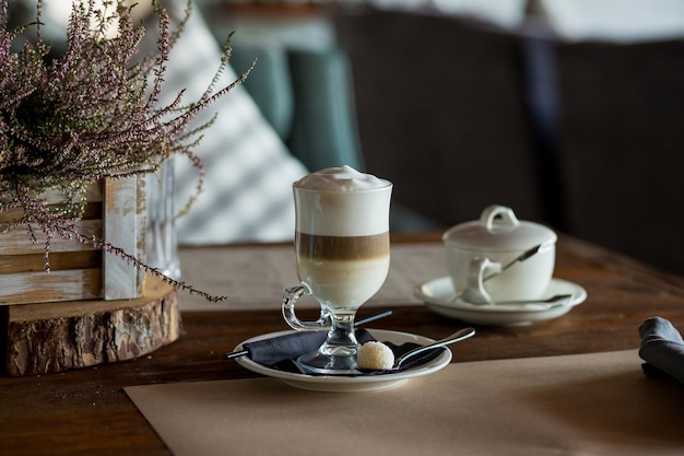 latte macchiato coffee with tasty foam clear glass on wooden table serving with cookie,cane sugar. 