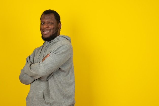 Laughing African American man standing with arms crossed , stands over yellow wall. 