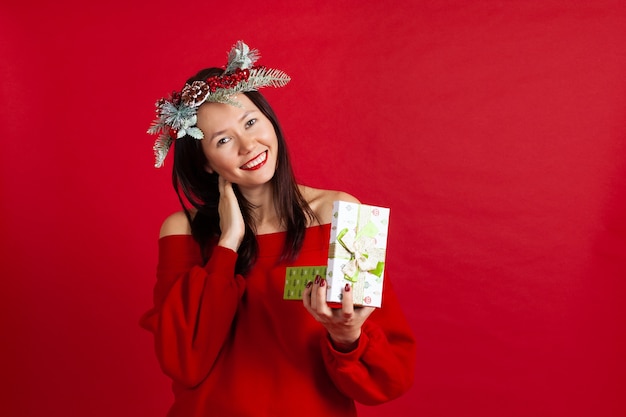 Laughing Asian woman in a Christmas wreath with red lipstick enjoying a new years gift