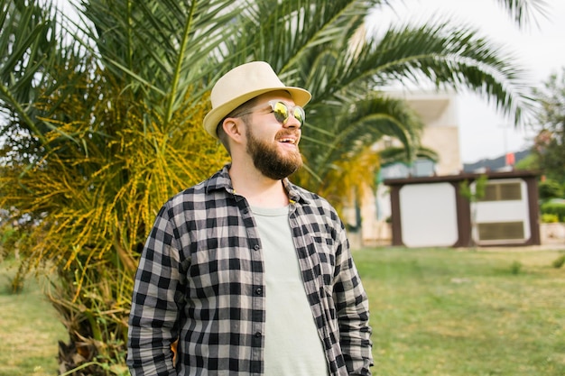 Laughing attractive man wearing hat over palm tree background with copy space emotion and vacation travel holidays concept