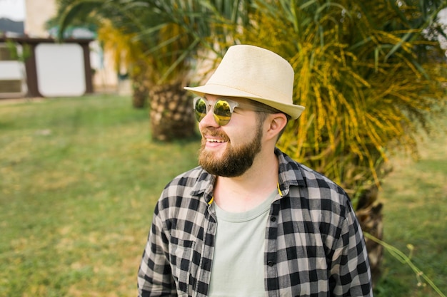 Laughing attractive man wearing hat over palm tree background with copy space emotion and vacation travel holidays concept