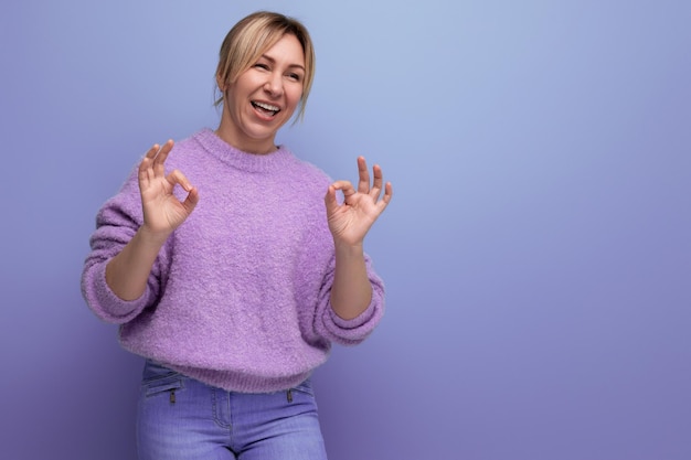 Laughing blonde young woman in a lilac sweater with a kind heart on a bright background with copy