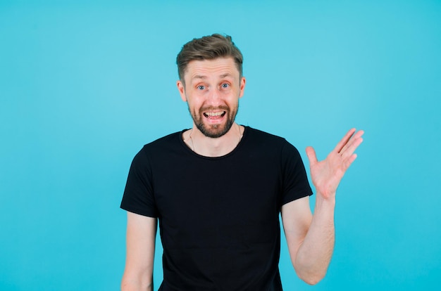 Laughing boy is looking at camera by pointing right with hand on blue background