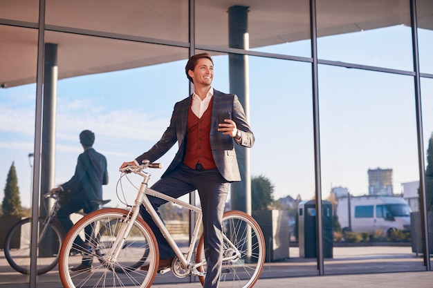 Laughing businessman with phone and bike on town street