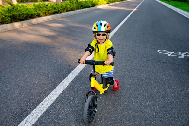 Laughing child in a protective helmet and sunglasses on a scooter on the road